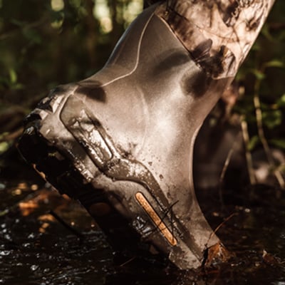 Waterproof rubber boot being worn by person walking through a creek
